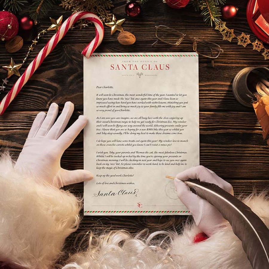 Santa signing a letter with a quill beside a candy cane
